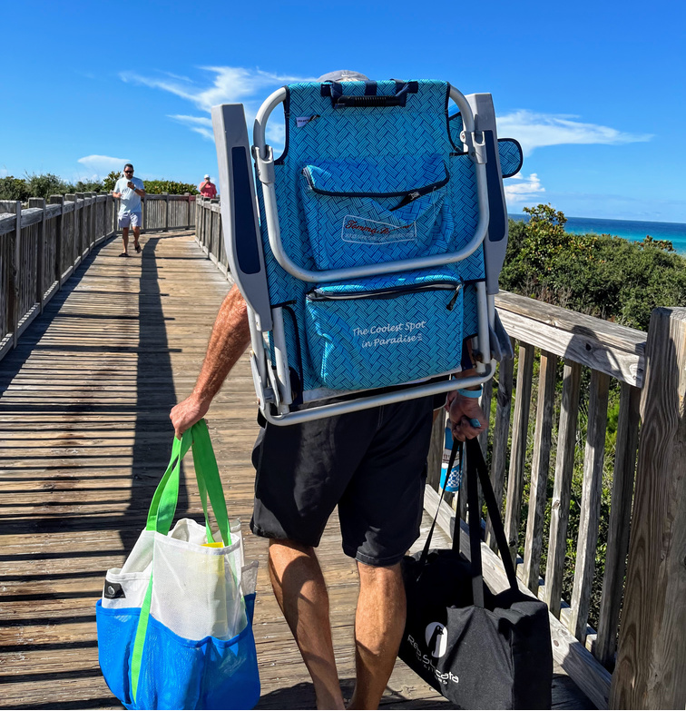 man carrying backpack beach chair and two beach bags